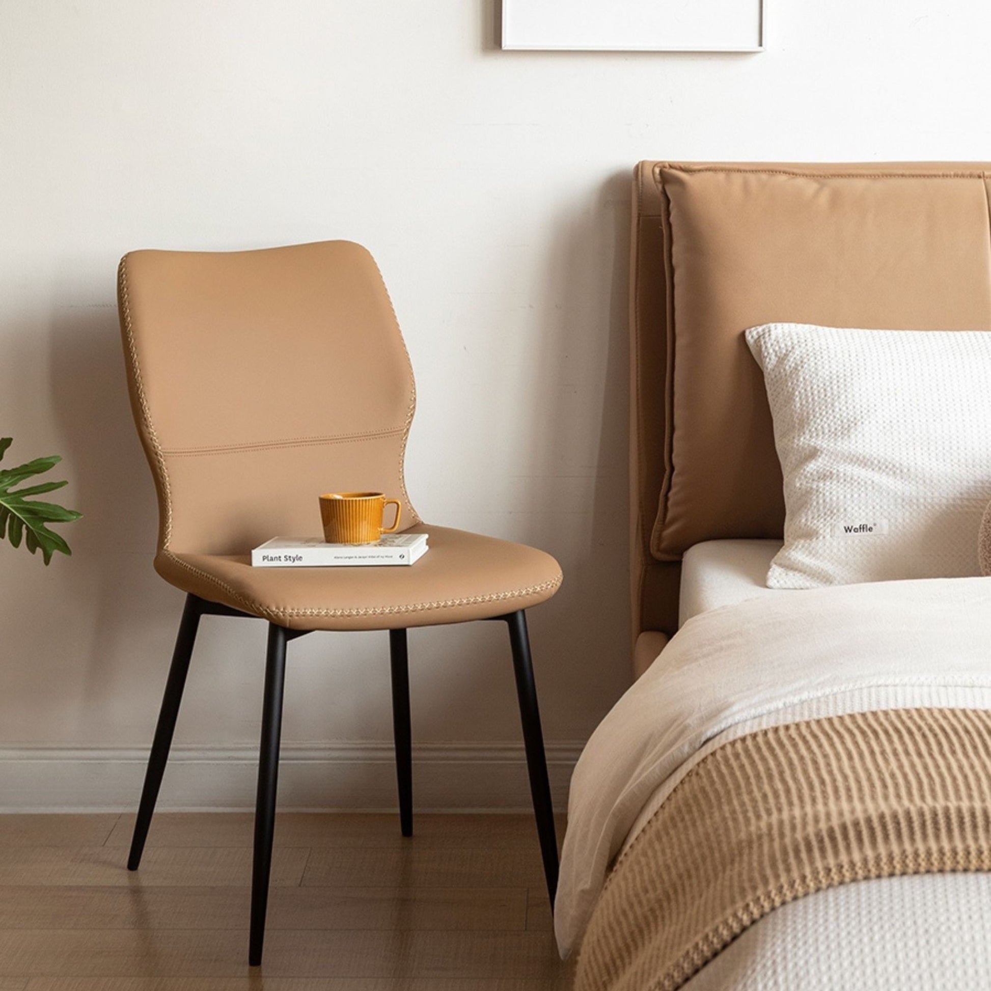 Brown chair with a cup and books next to a bed with a brown headboard and white bedding.
