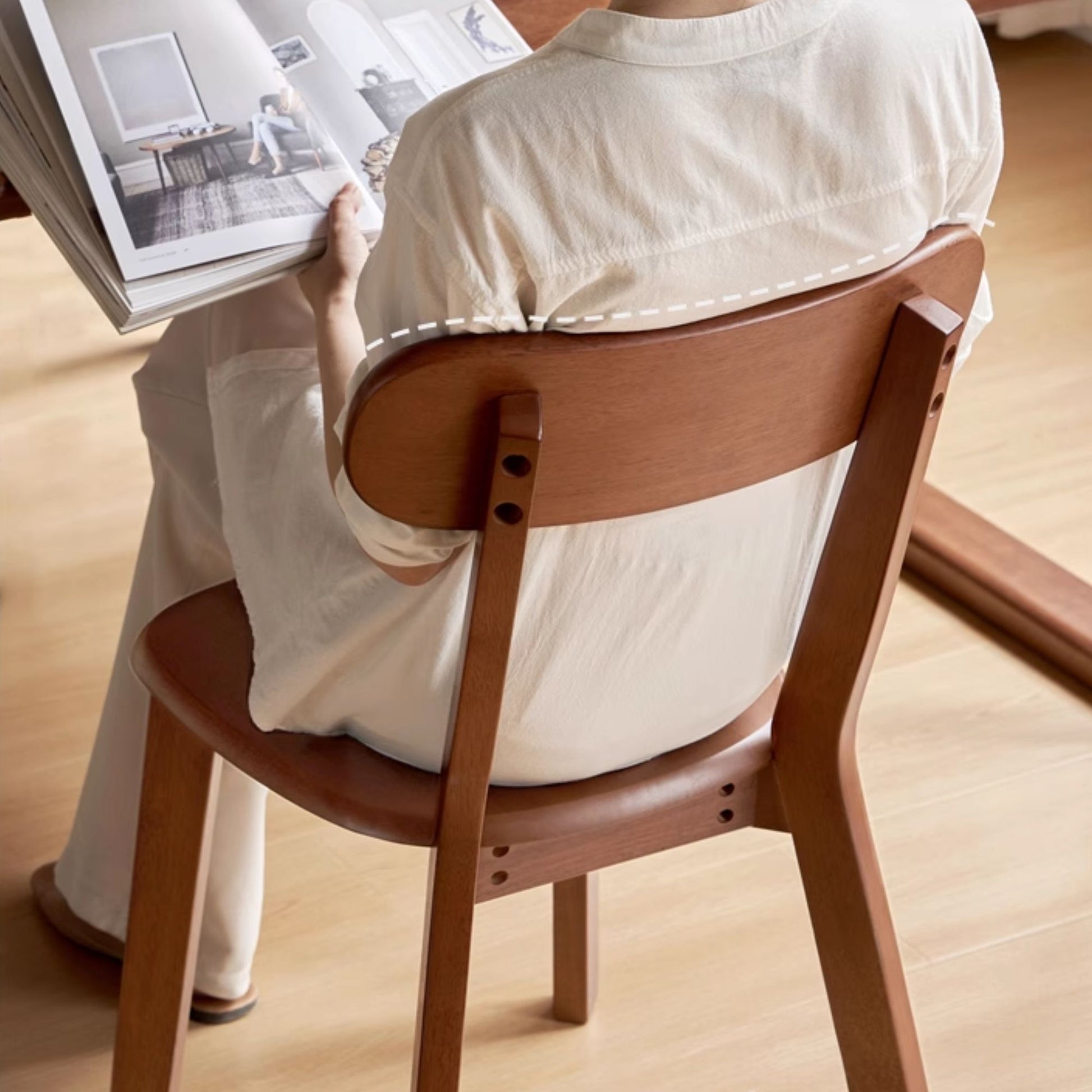 Person sitting on a wooden chair reading a book in a minimalistic setting