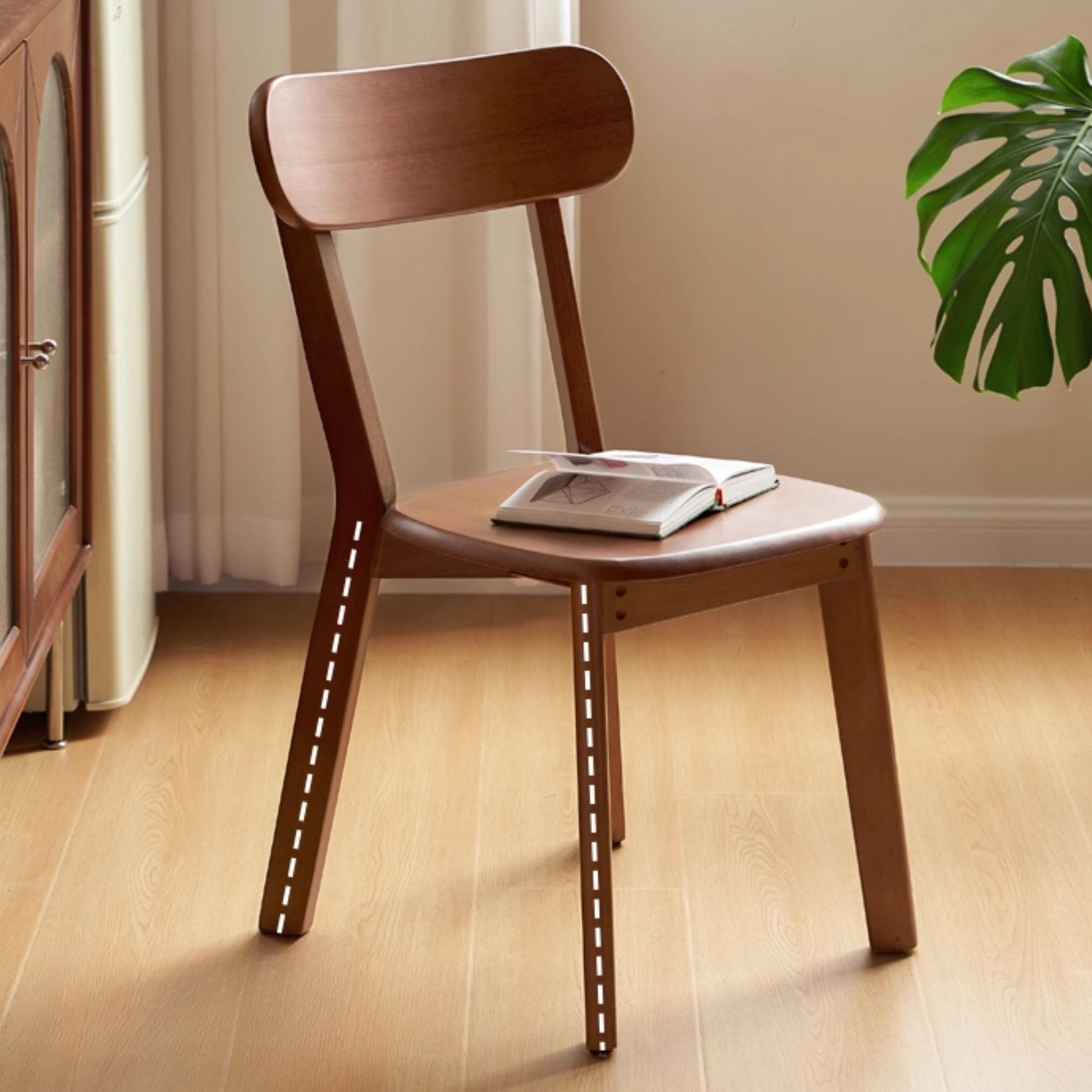 Wooden chair with a book on a wooden floor in a room with a plant.