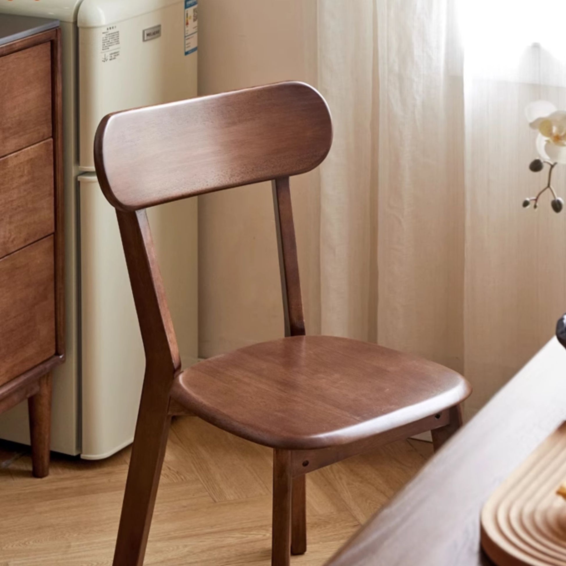 Wooden chair in a room with a refrigerator and curtains.