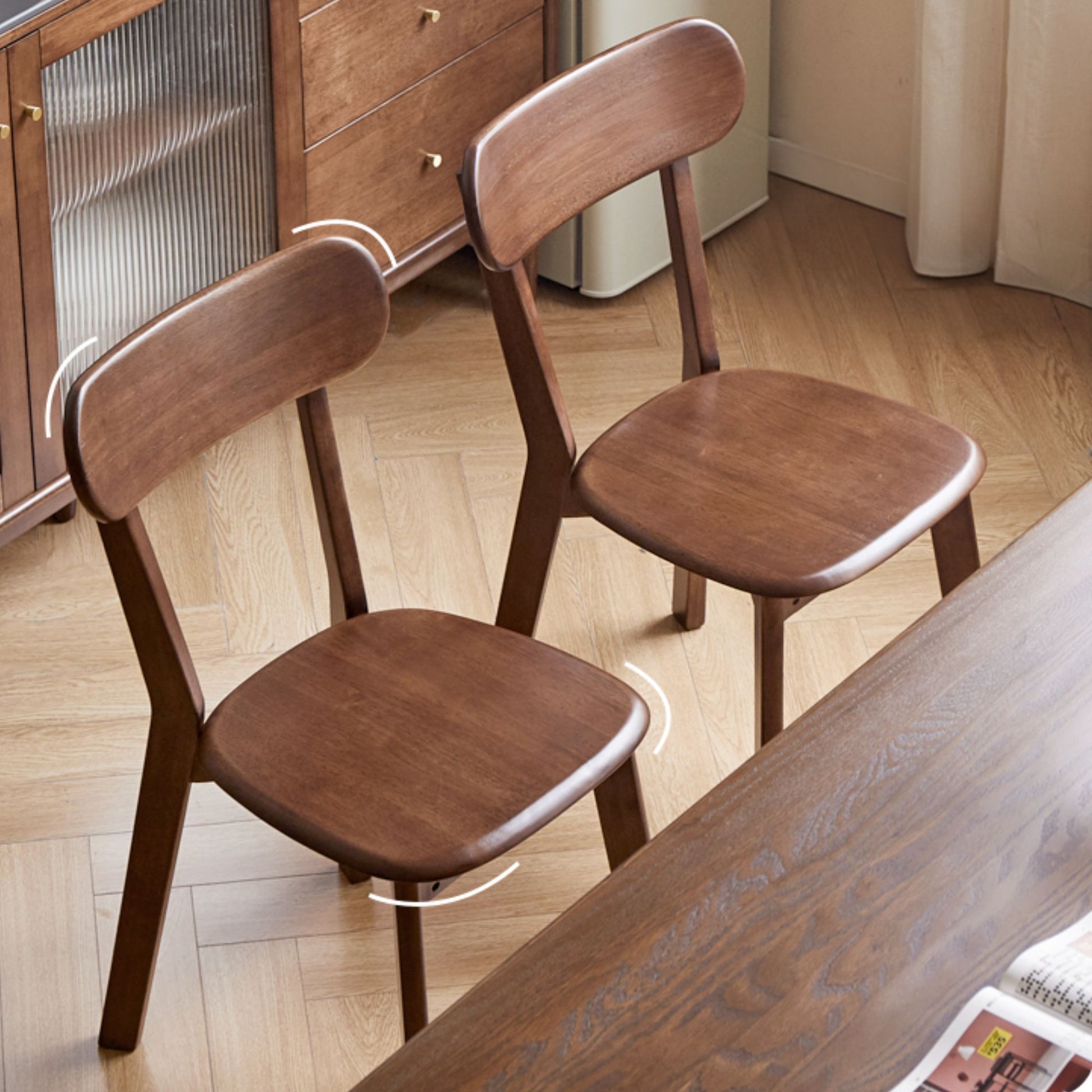 Two wooden chairs in a room with a table and cabinet.
