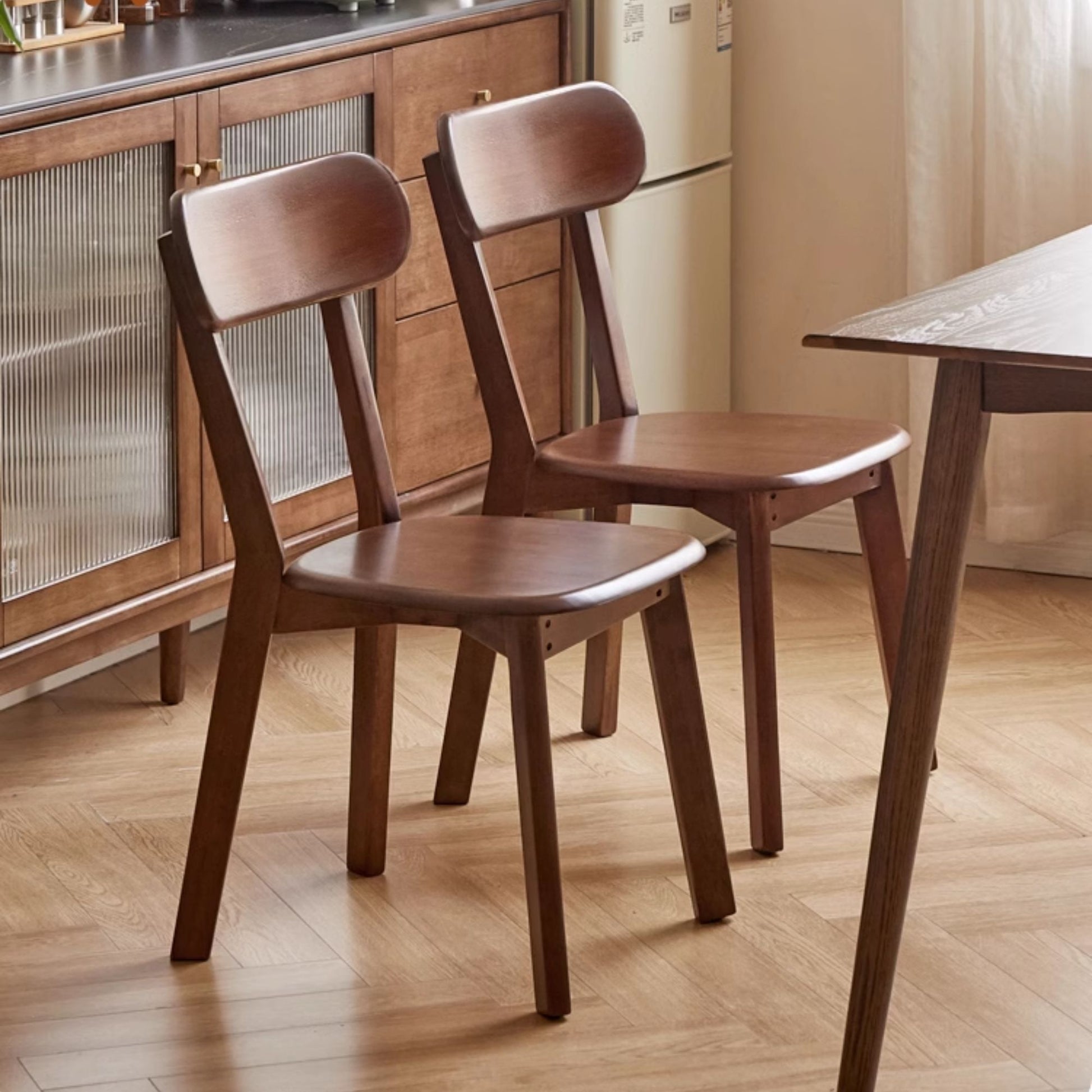 Two wooden chairs in a kitchen setting with a table and cabinets.