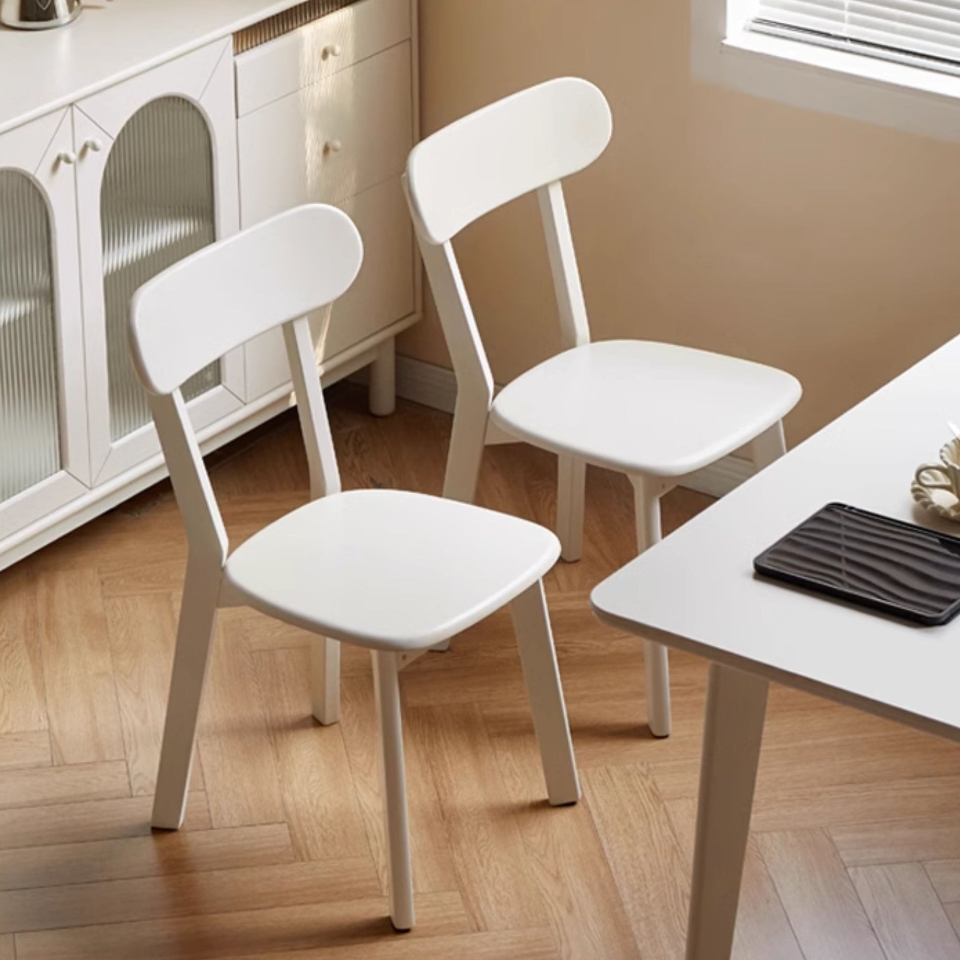 Two white chairs in a kitchen setting with a table and cabinets.