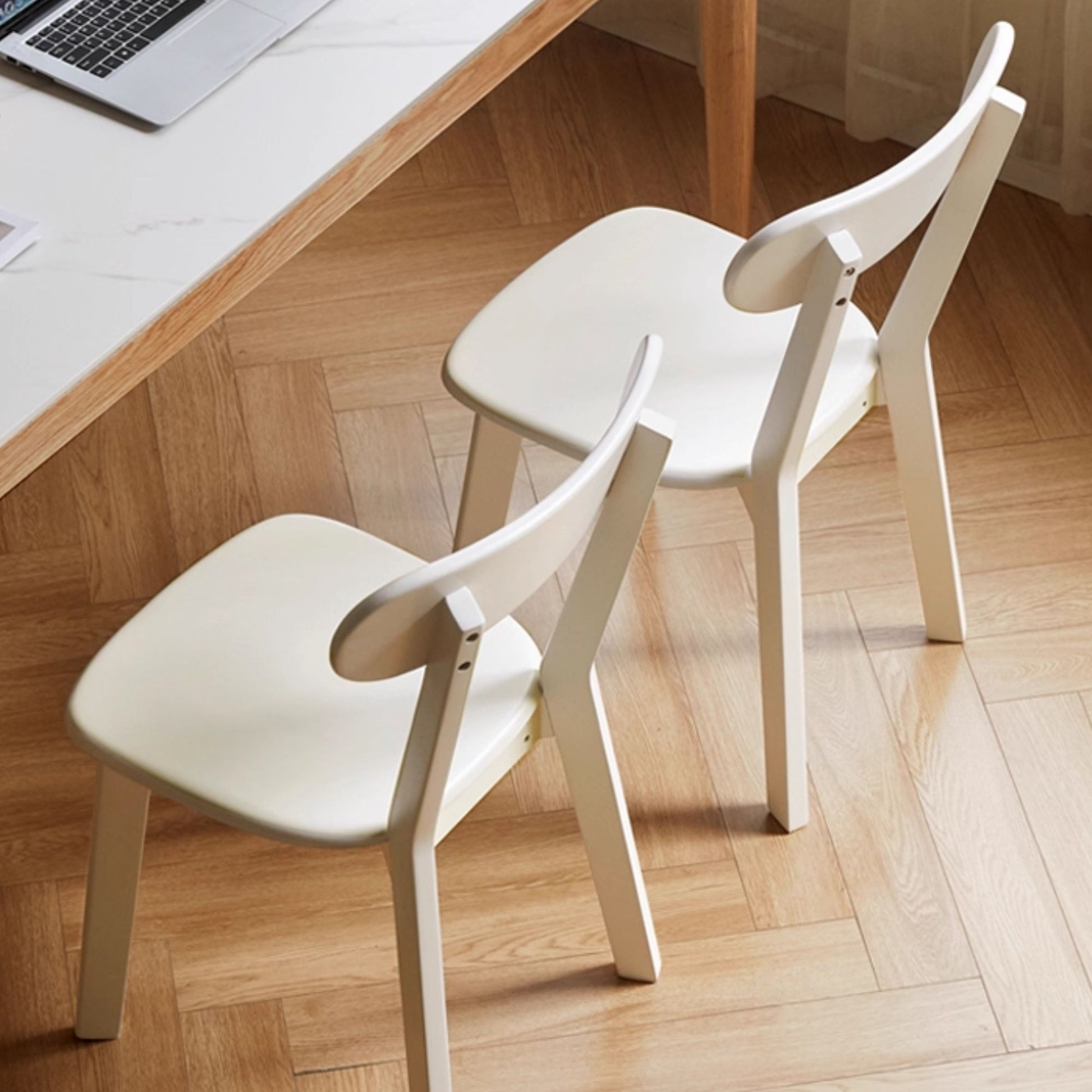 Two white chairs in front of a wooden desk with a laptop.