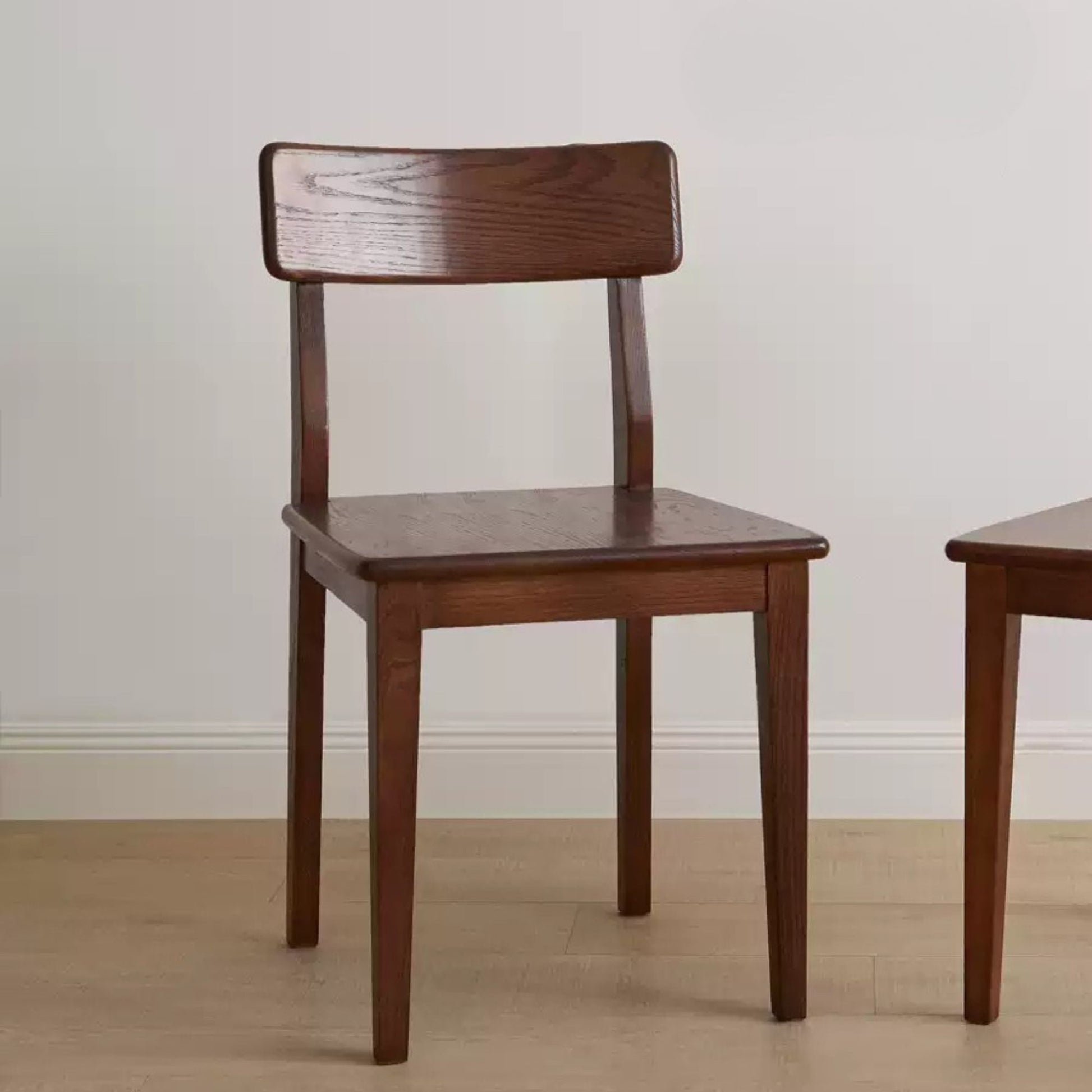 Wooden chair against a plain wall with another chair partially visible.