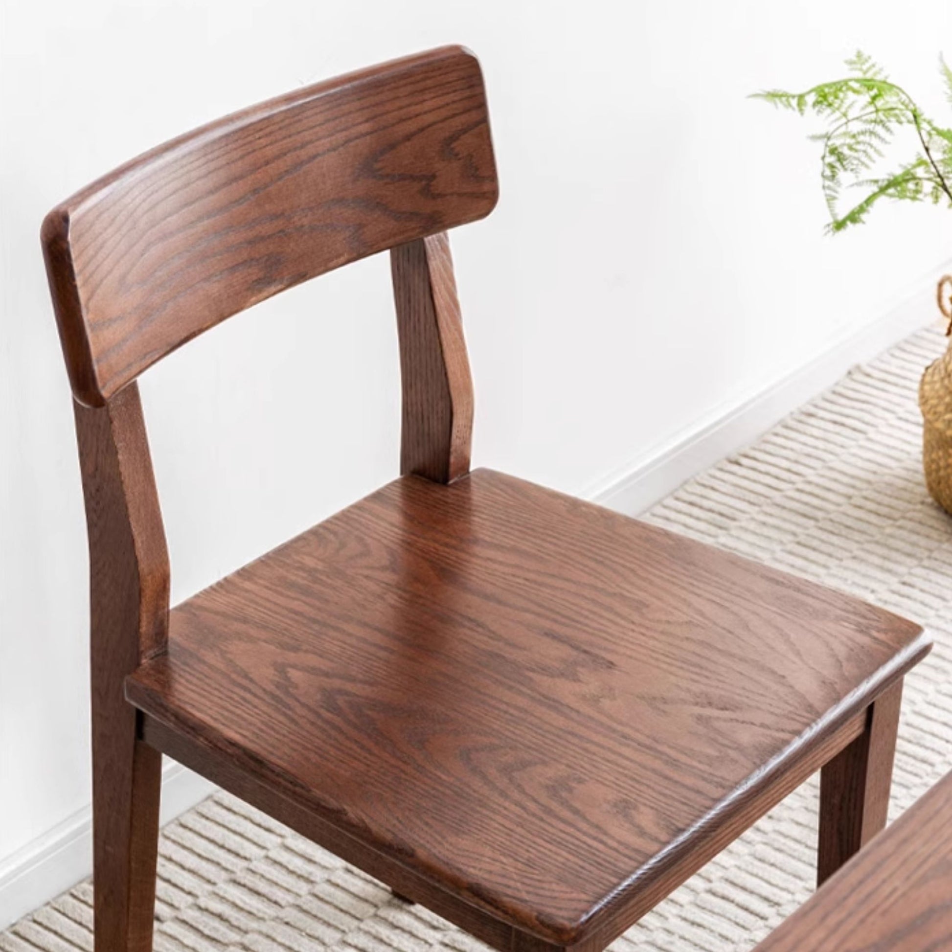 Wooden chair with a plant in the background on a light-colored floor.