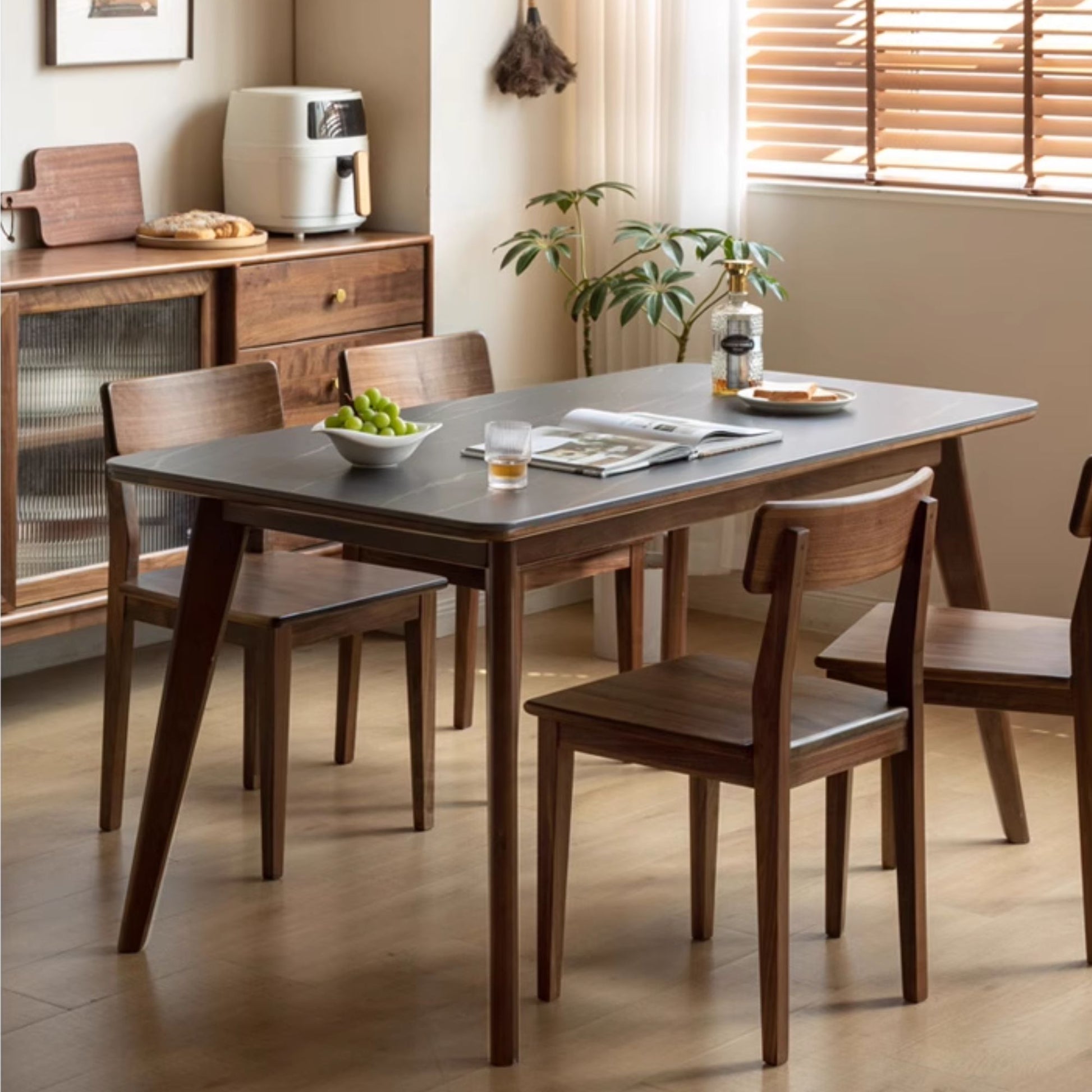 Dining room with wooden table and chairs, plants, and a window with blinds.