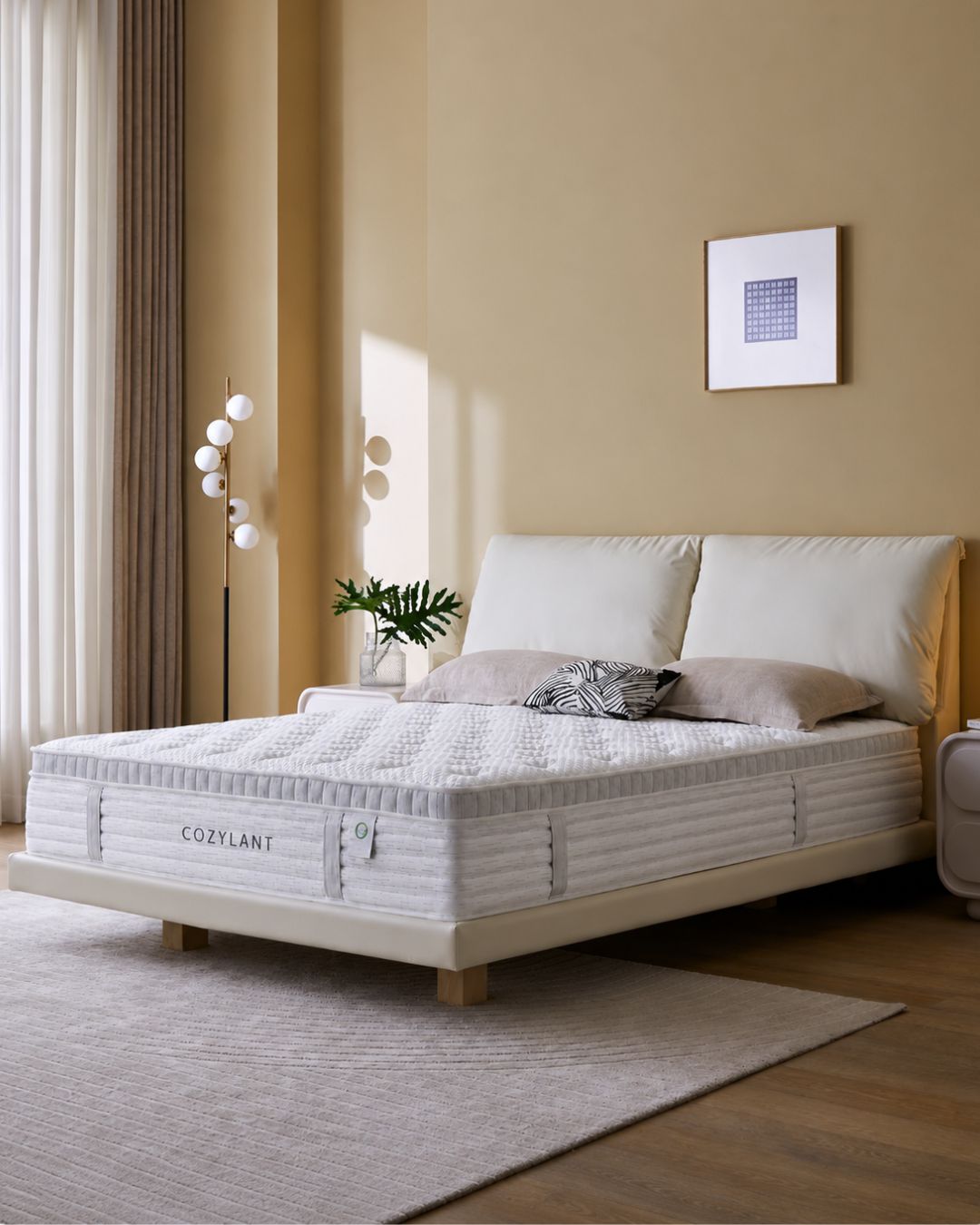 A CozyLant mattress shown on a bed in a modern, warm-toned bedroom. The mattress is white with quilted and ribbed textures, resting on a light wood bed frame with white headboard and a patterned accent pillows.