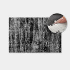 A rectangular rug or mat with a distressed black, gray, and white vertical textured pattern, shown on a light gray background with a circular inset demonstrating the soft pile texture.