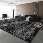 A large rectangular area rug with a distressed black and white abstract pattern, shown in a modern living room setting with a dark gray sectional sofa, black accent chair, and gray tiled floor.