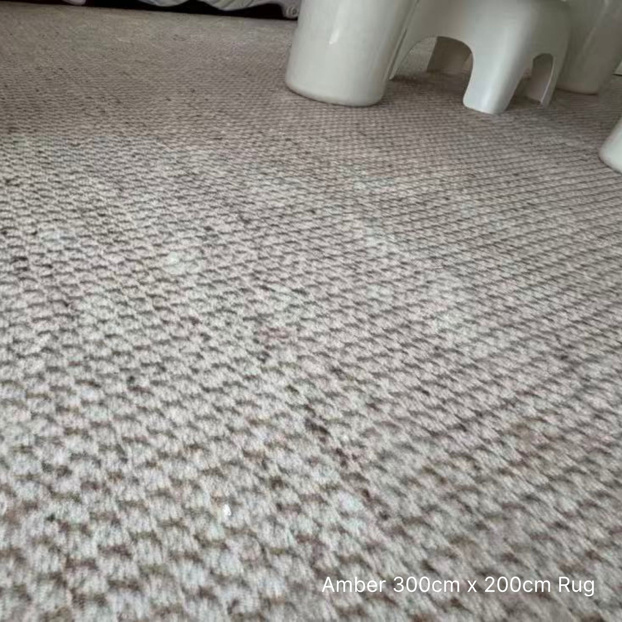 Close-up of a textured rug with a white stool partially visible.
