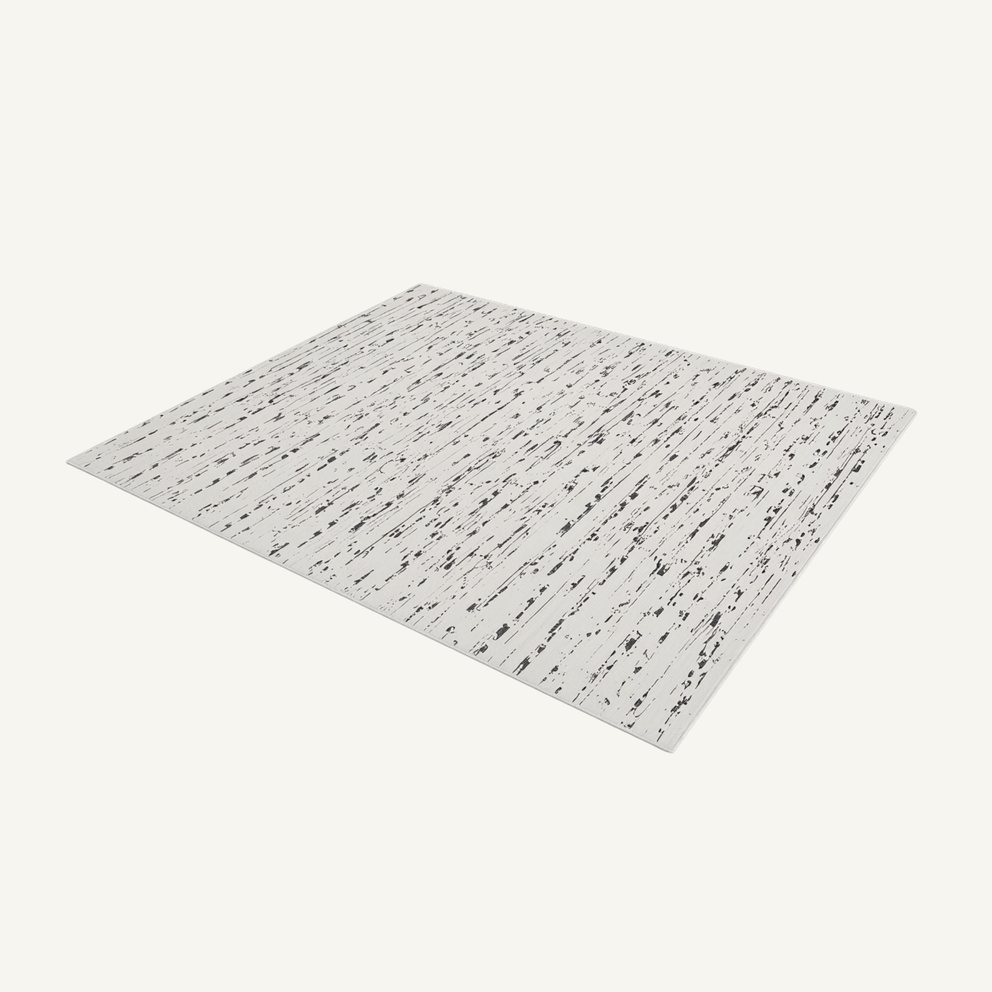 A rectangular area rug with a distressed white background and black speckled, birch-wood style markings, shown at an angle on a light off-white background.