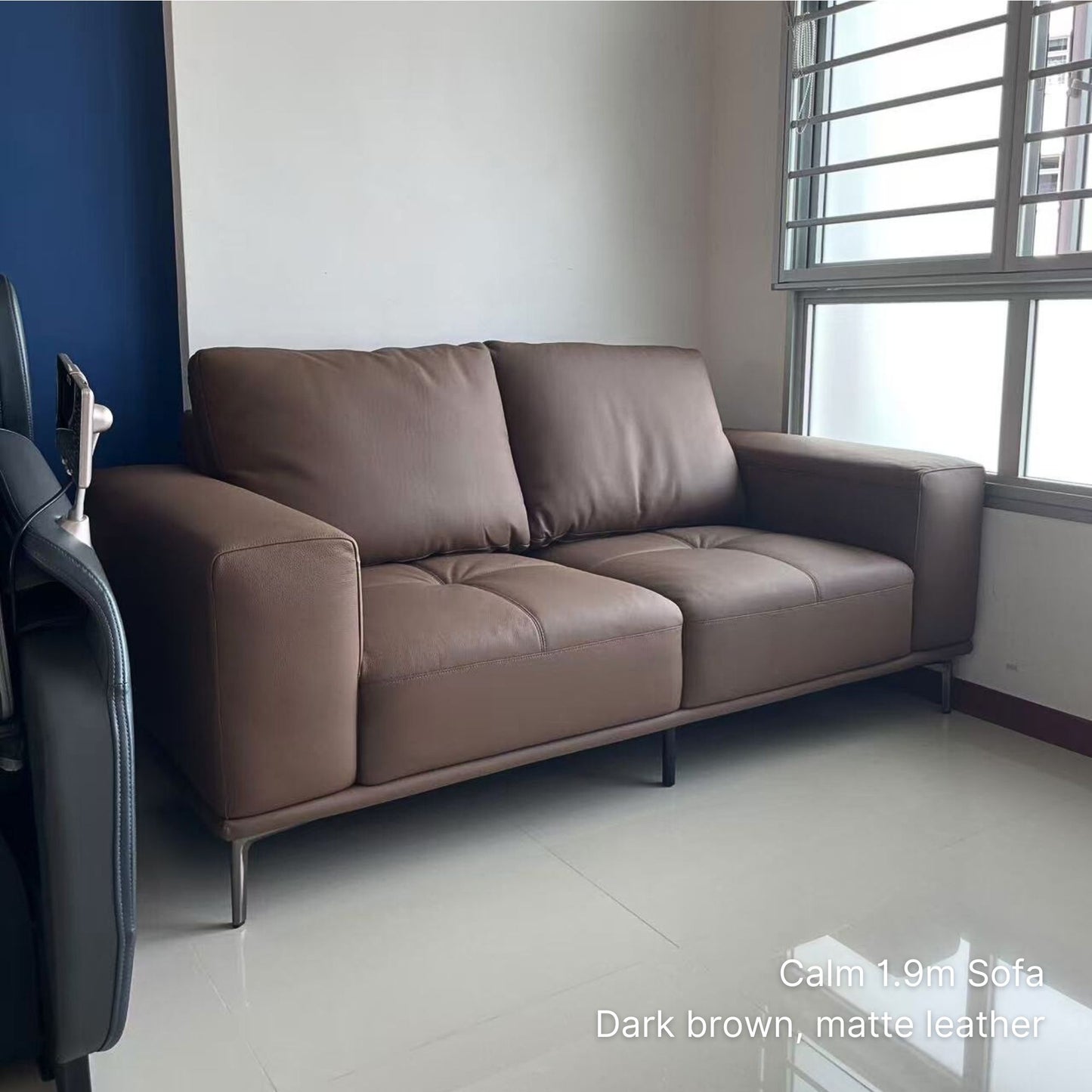 Dark brown sofa in a room with a window and blue wall.