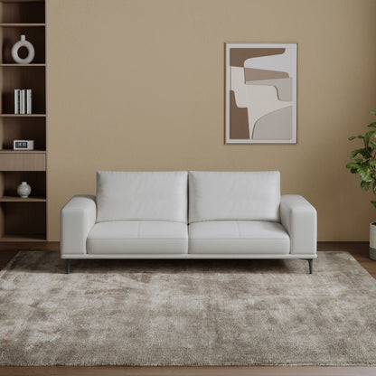 White leather sofa in a living room with a abstract painting on the wall and a plant.