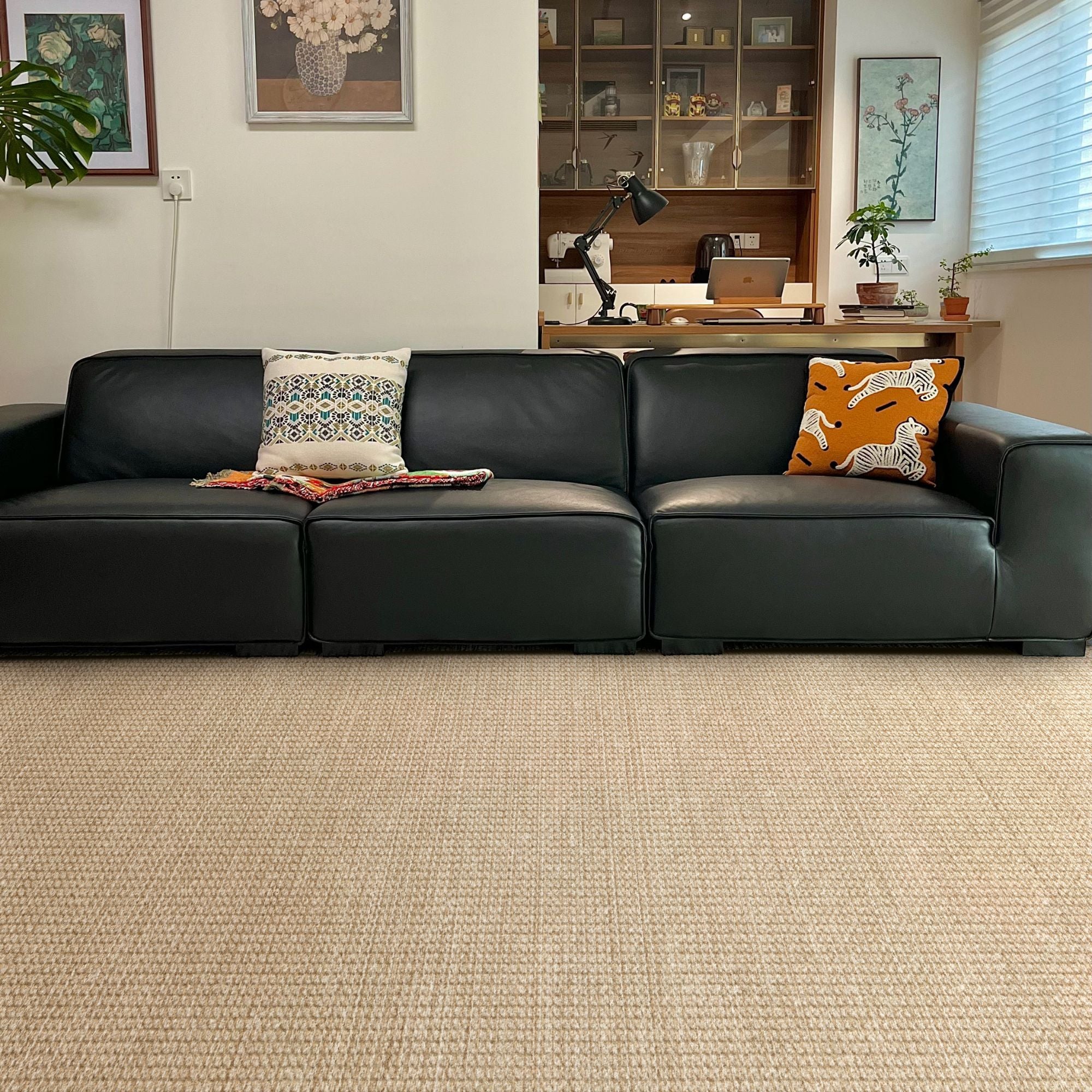 A modern black leather sectional sofa in a living room setting, featuring two decorative throw pillows and a folded blanket, set on a textured beige woven rug.