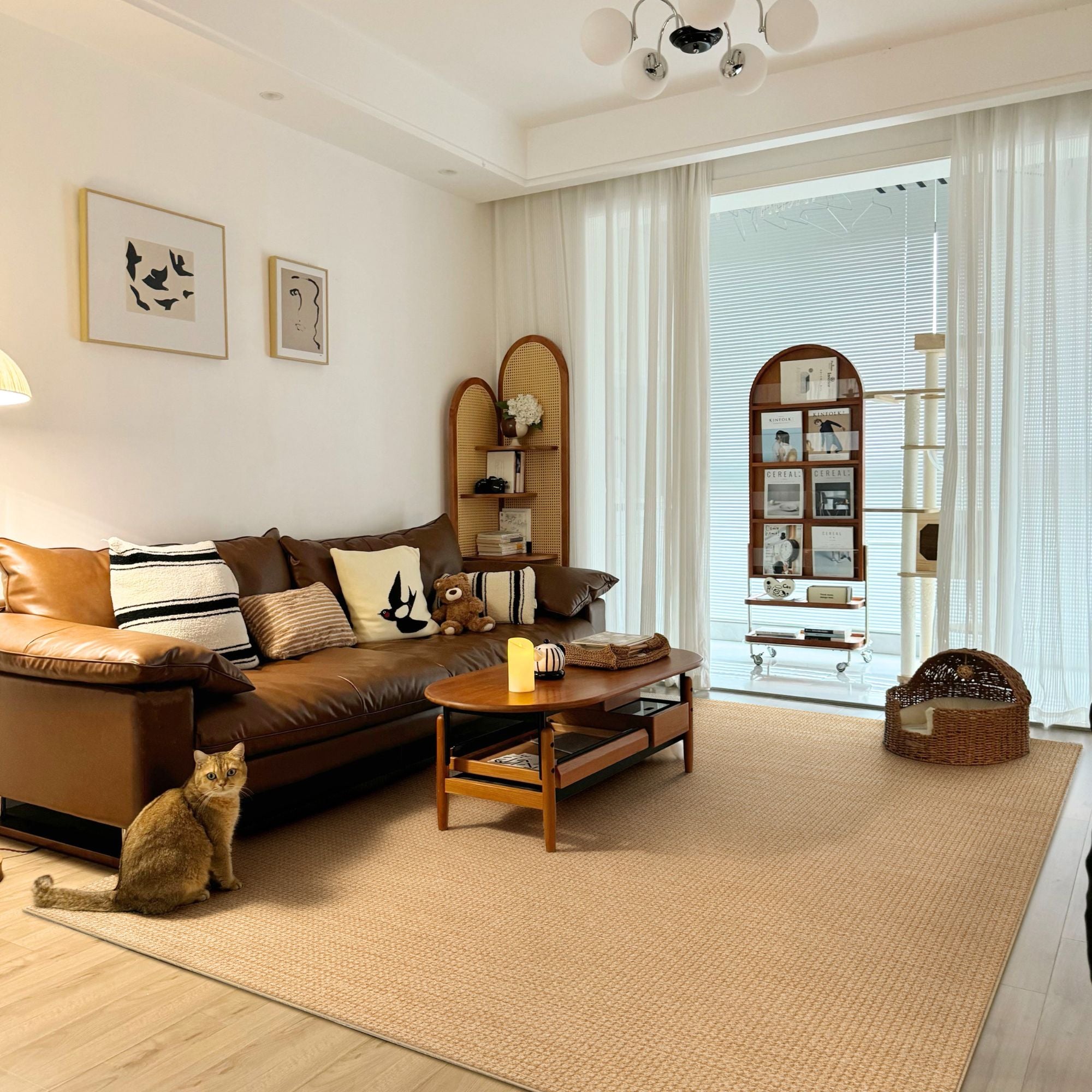 A warm, modern living room featuring a large beige textured area rug as the main flooring. A brown leather sofa with striped and cream pillows sits on the rug next to a small orange tabby cat.