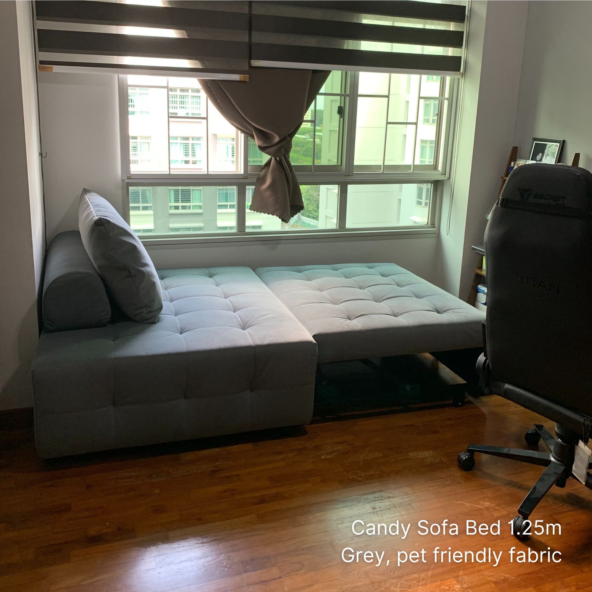 Gray sofa bed in a room with a window and chair.
