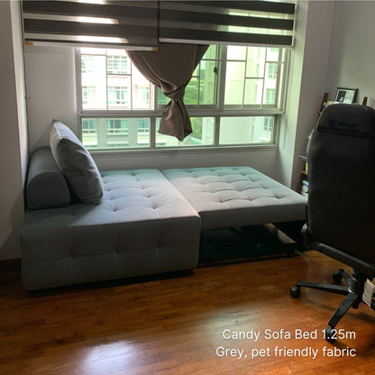 Gray sofa bed in a room with a window and chair.