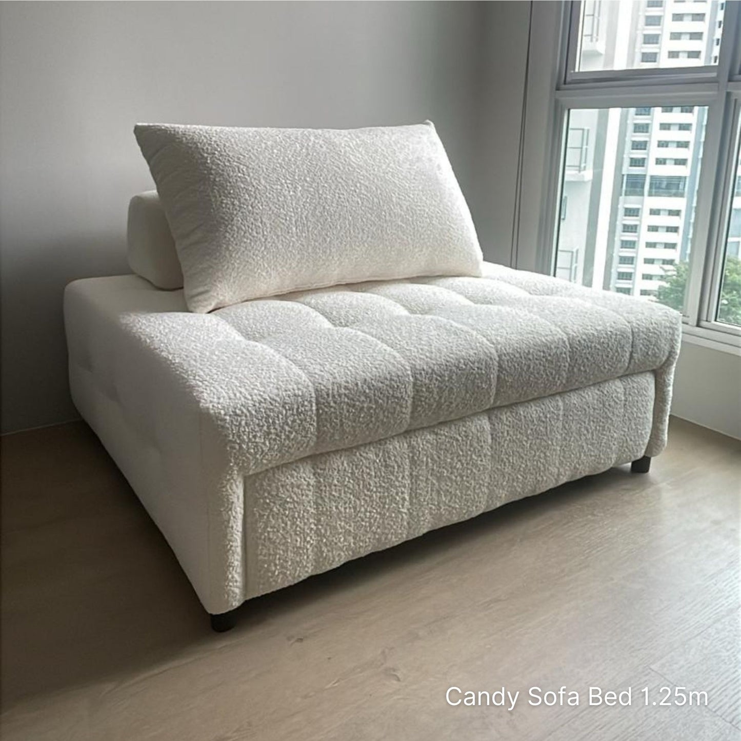 White sofa bed with a pillow in a room with large windows.