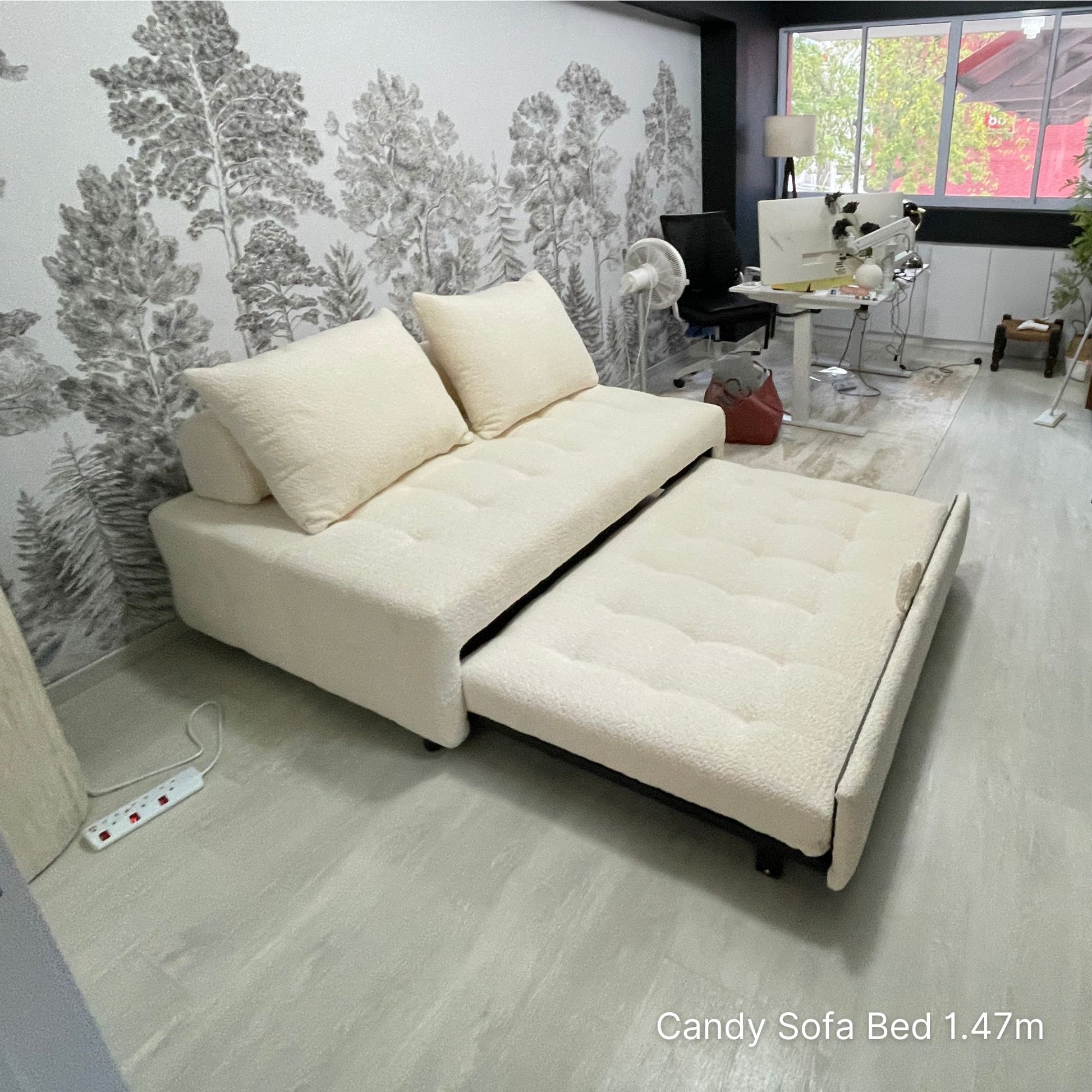 White sofa bed in a room with a forest wallpaper and a small table.