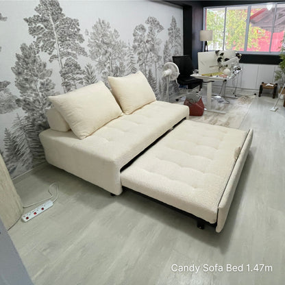 White sofa bed in a room with a forest wallpaper and a small table.