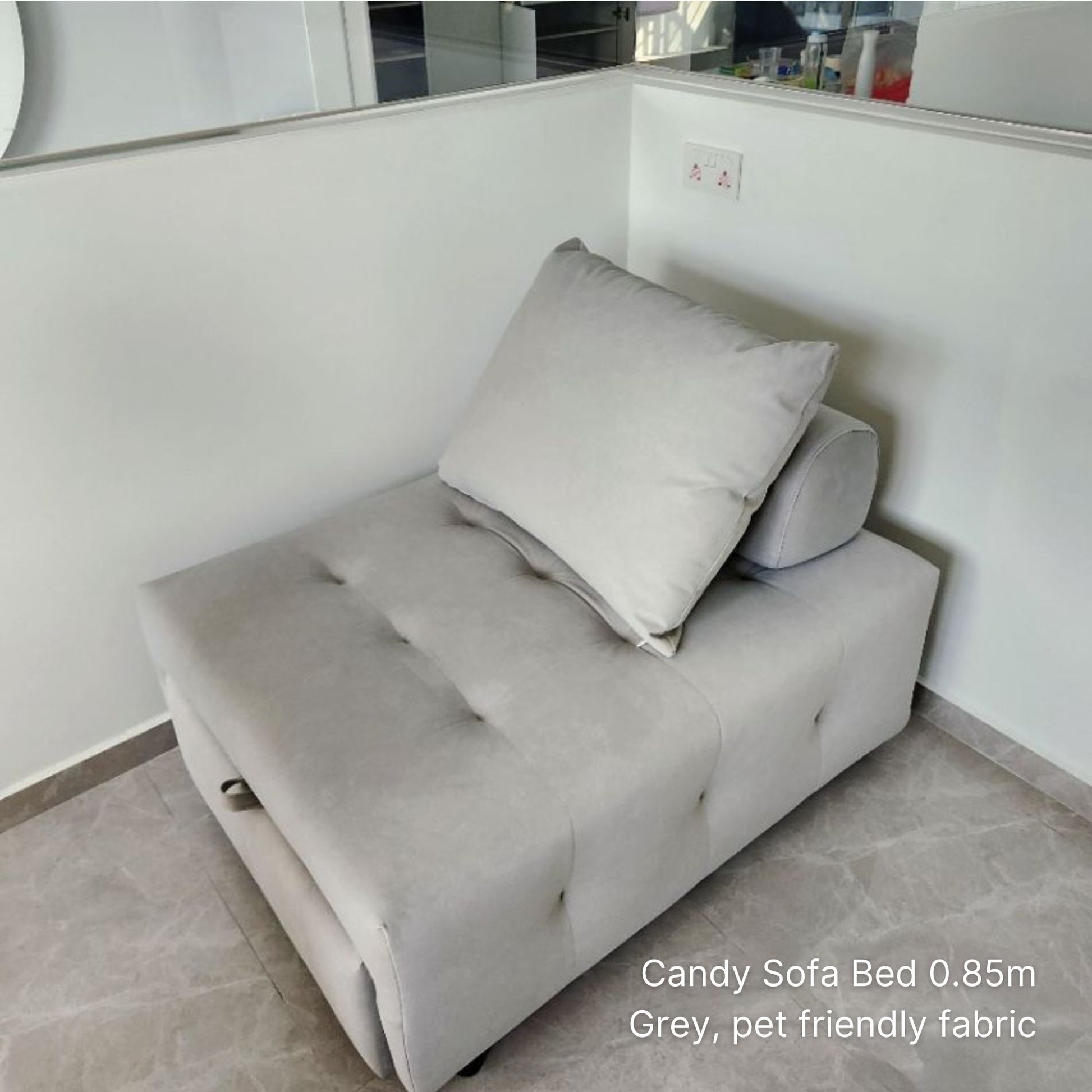 Gray sofa bed with a pillow in a room with white walls and a tiled floor.