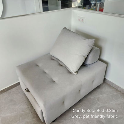 Gray sofa bed with a pillow in a room with white walls and a tiled floor.