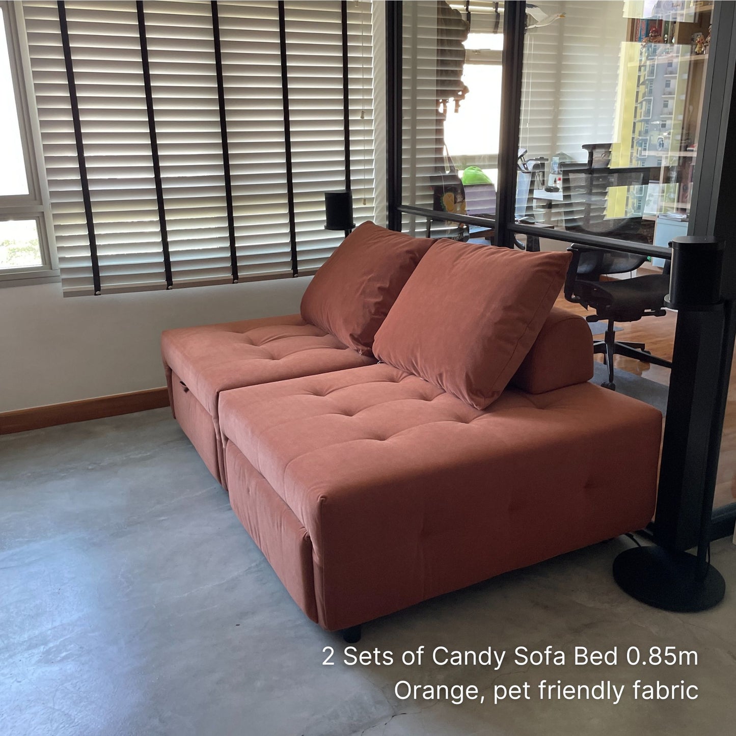 Orange sofa bed in a room with large windows and a chair.