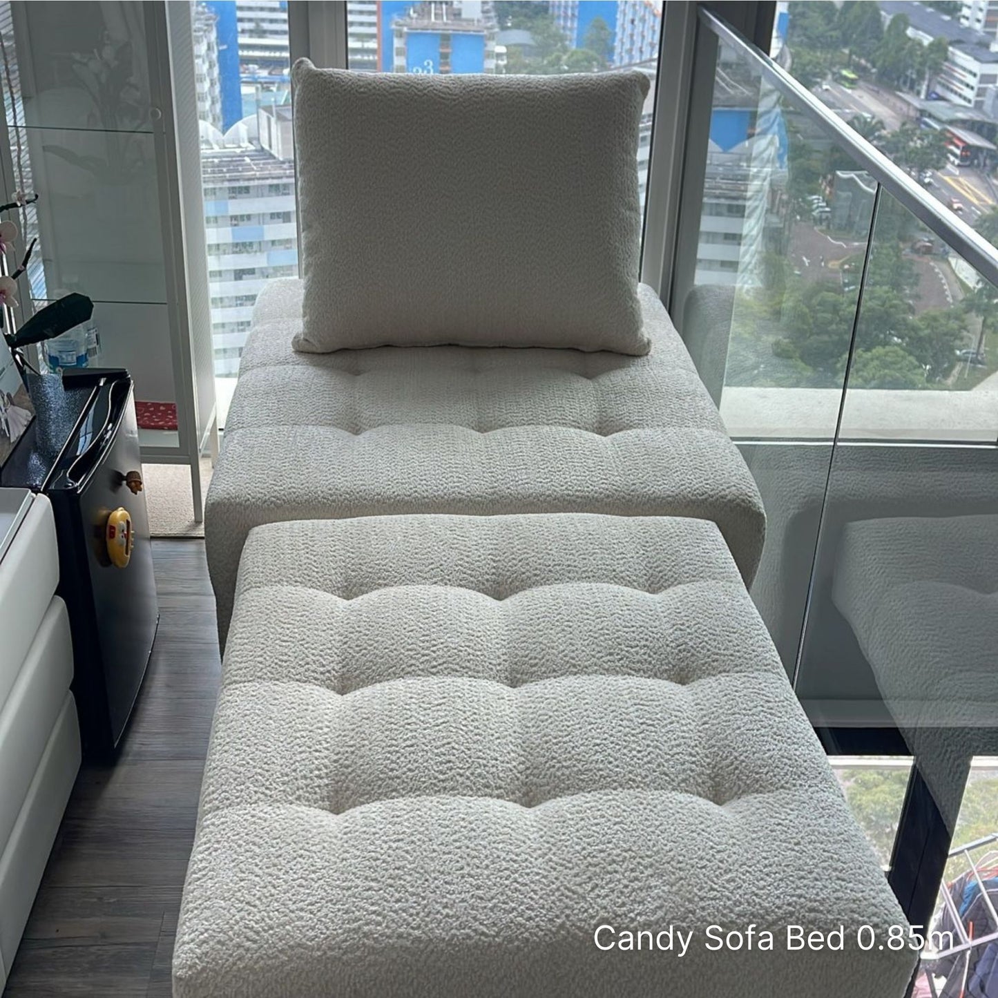 White sofa bed with a pillow in a room with large windows showing an urban view.