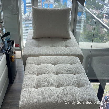 White sofa bed with a pillow in a room with large windows showing an urban view.
