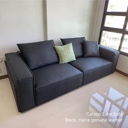 Black 3 seater 240cm Carson leather sofa with a green pillow in a room with large windows.