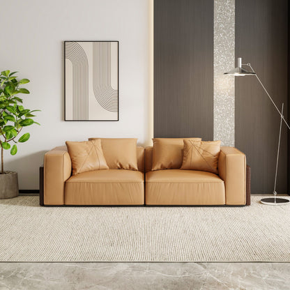 Brown leather sofa in a modern living room with a plant and abstract art on the wall.
