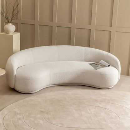 Modern white sofa against a beige paneled wall with a small table and decorative vase.