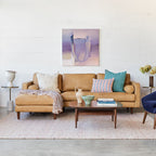 Living room with a brown faux leather sectional sofa, coffee table, and abstract painting on a white wall.
