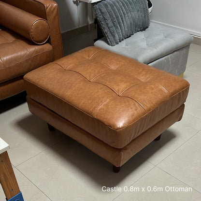 Brown leather ottoman in a room with tiled floor and brown sofa.
