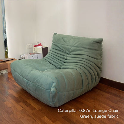 Green suede fabric Caterpillar lounge chair on a wooden floor with a neutral wall background