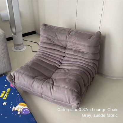 Gray suede fabric Caterpillar lounge chair against a white wall with a colorful mat on the floor.