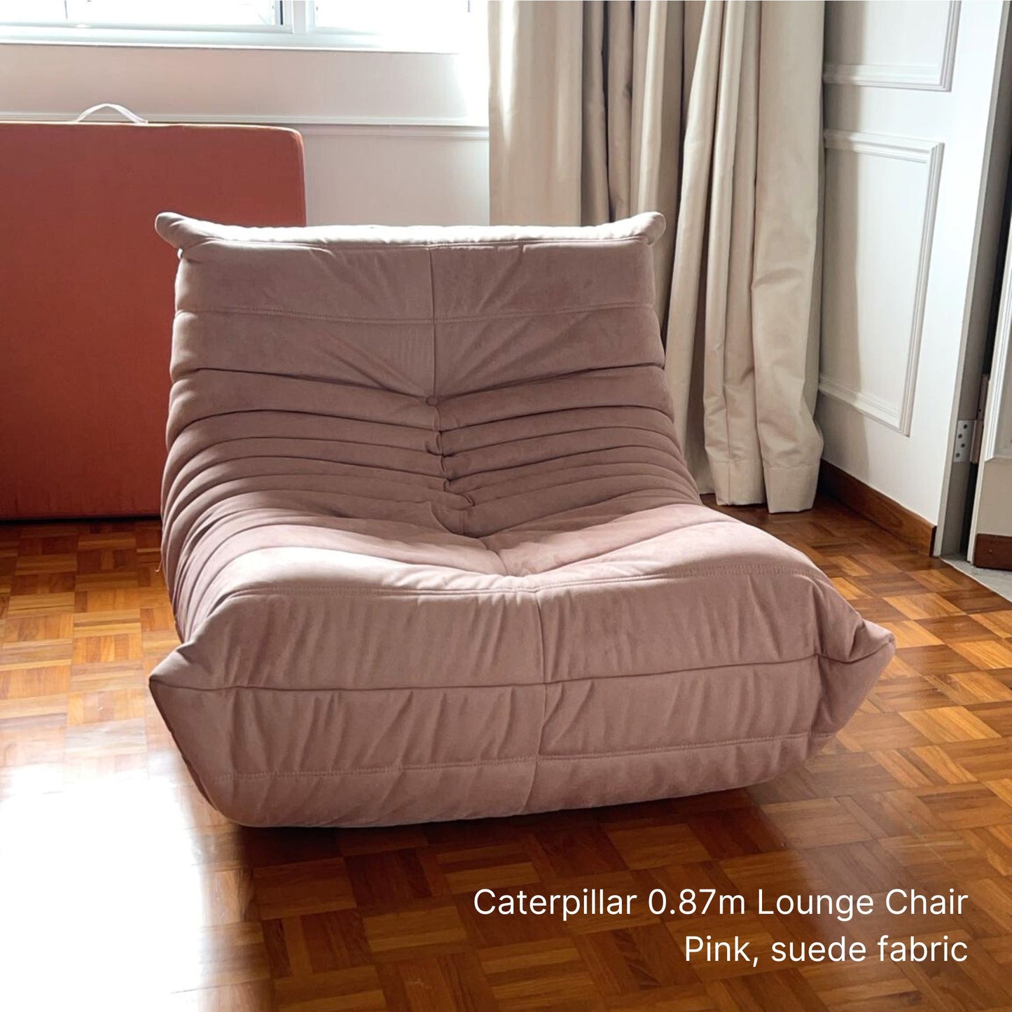 Pink suede lounge chair on a wooden floor with curtains in the background