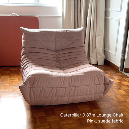Pink suede lounge chair on a wooden floor with curtains in the background