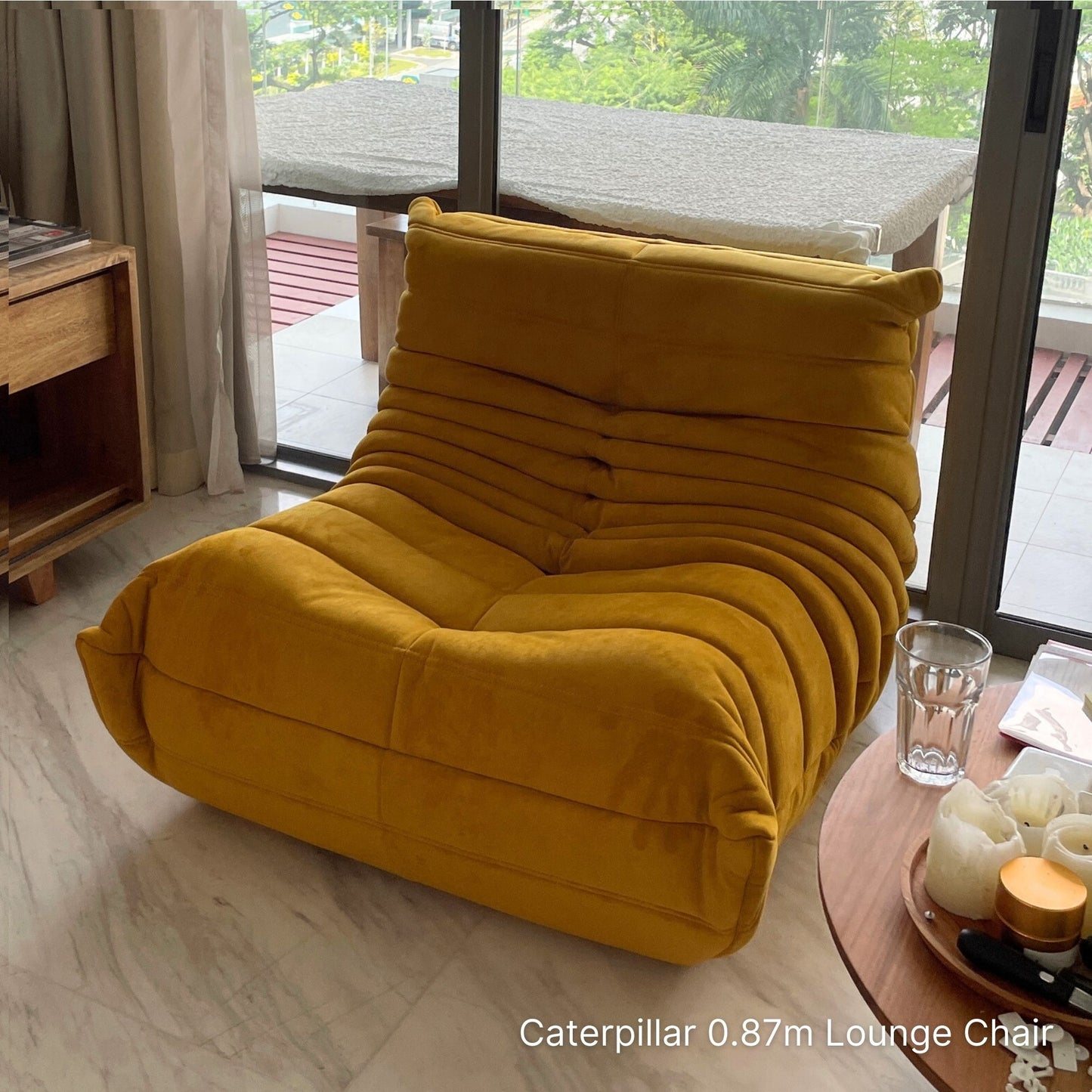 Yellow lounge chair in a living room setting with a glass of water and candles on a table.