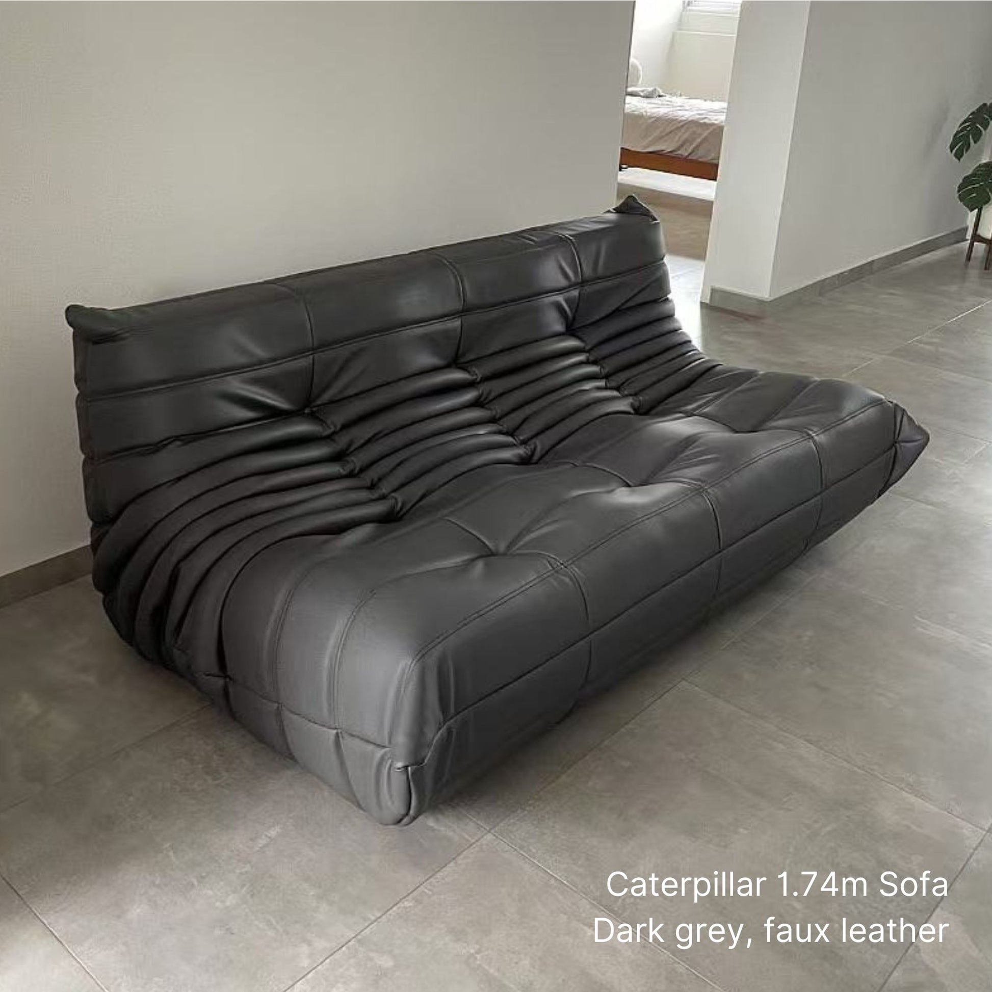Dark grey 174cm 3 seater faux leather Caterpillar sofa on a tiled floor with a neutral wall background