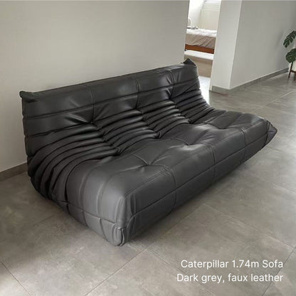 Dark grey 174cm 3 seater faux leather Caterpillar sofa on a tiled floor with a neutral wall background