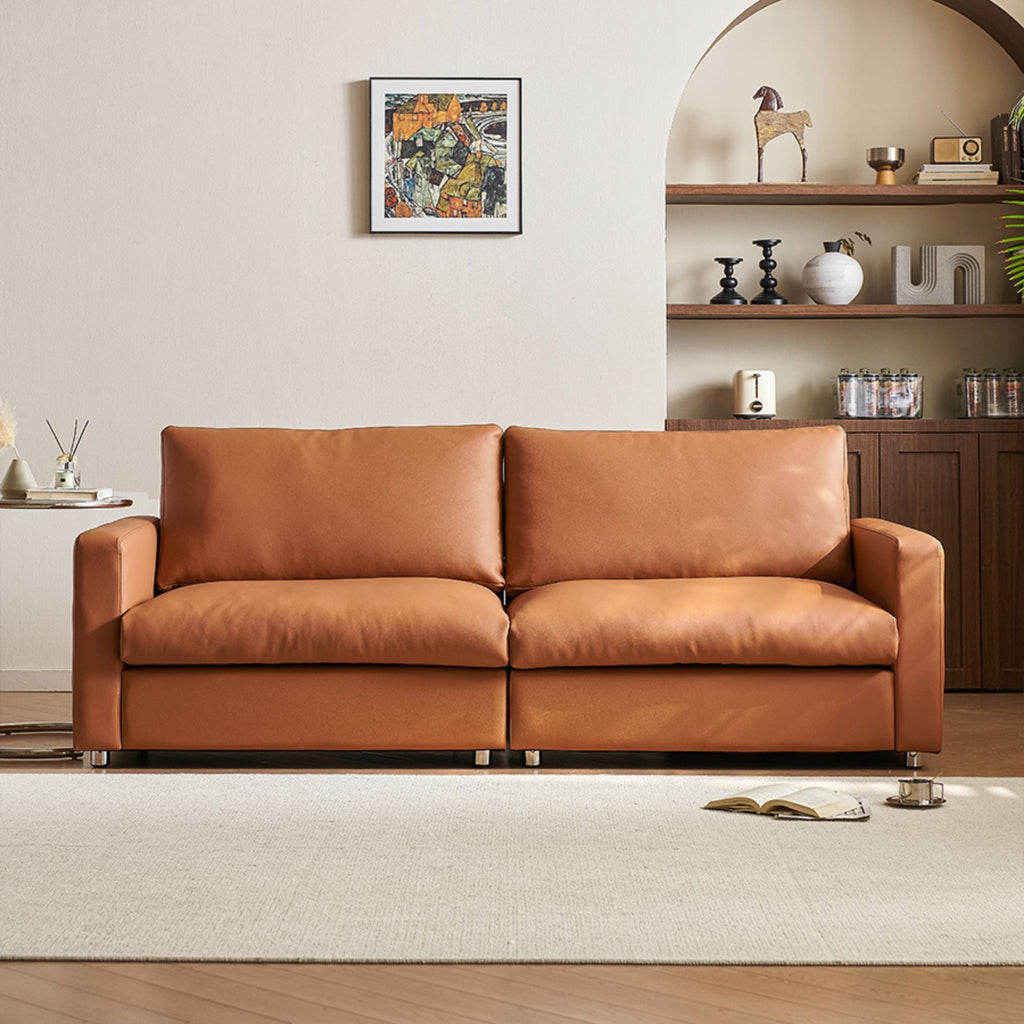Brown leather sofa in a living room with a shelf and artwork in the background.