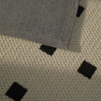 Close-up of a textured rug with black square patterns on a beige background