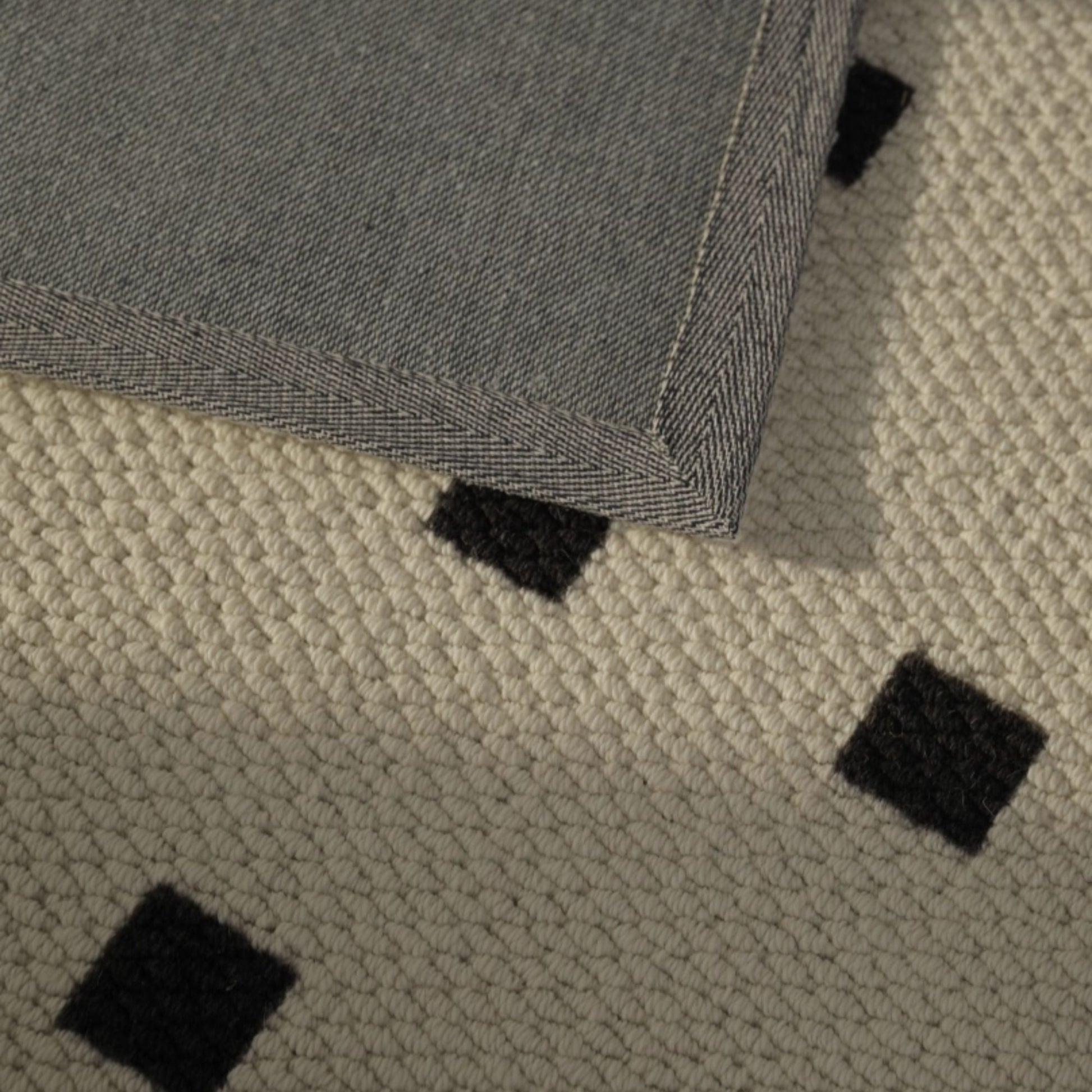 Close-up of a textured rug with black square patterns on a beige background