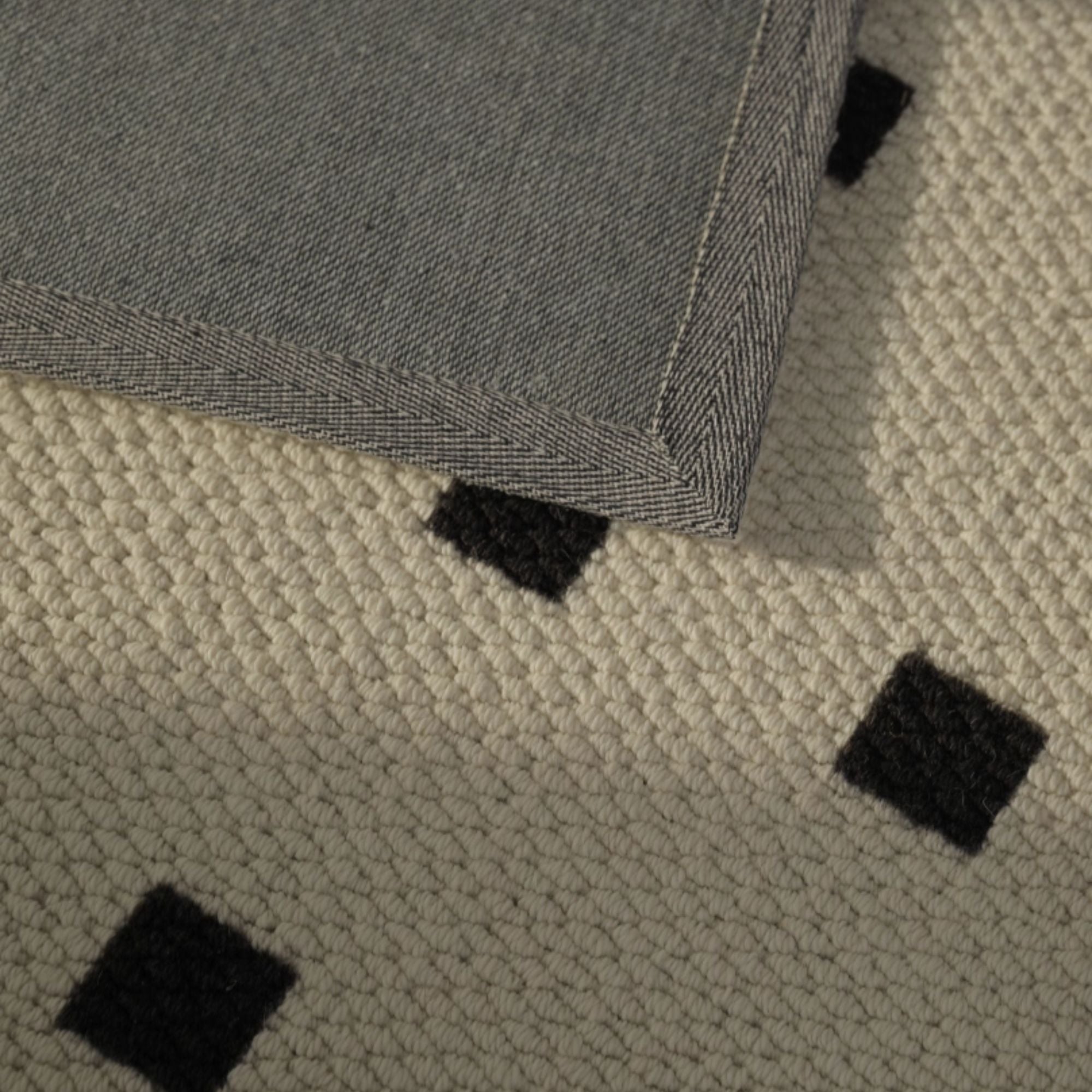 Close-up of a textured rug with black square patterns on a beige background