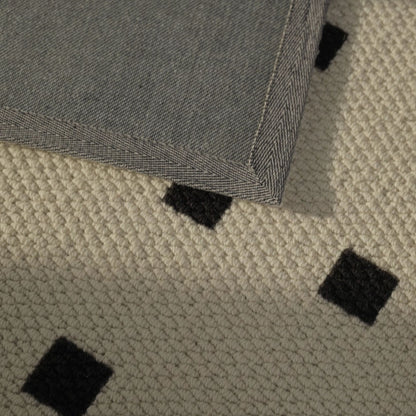 Close-up of a textured rug with black square patterns on a beige background