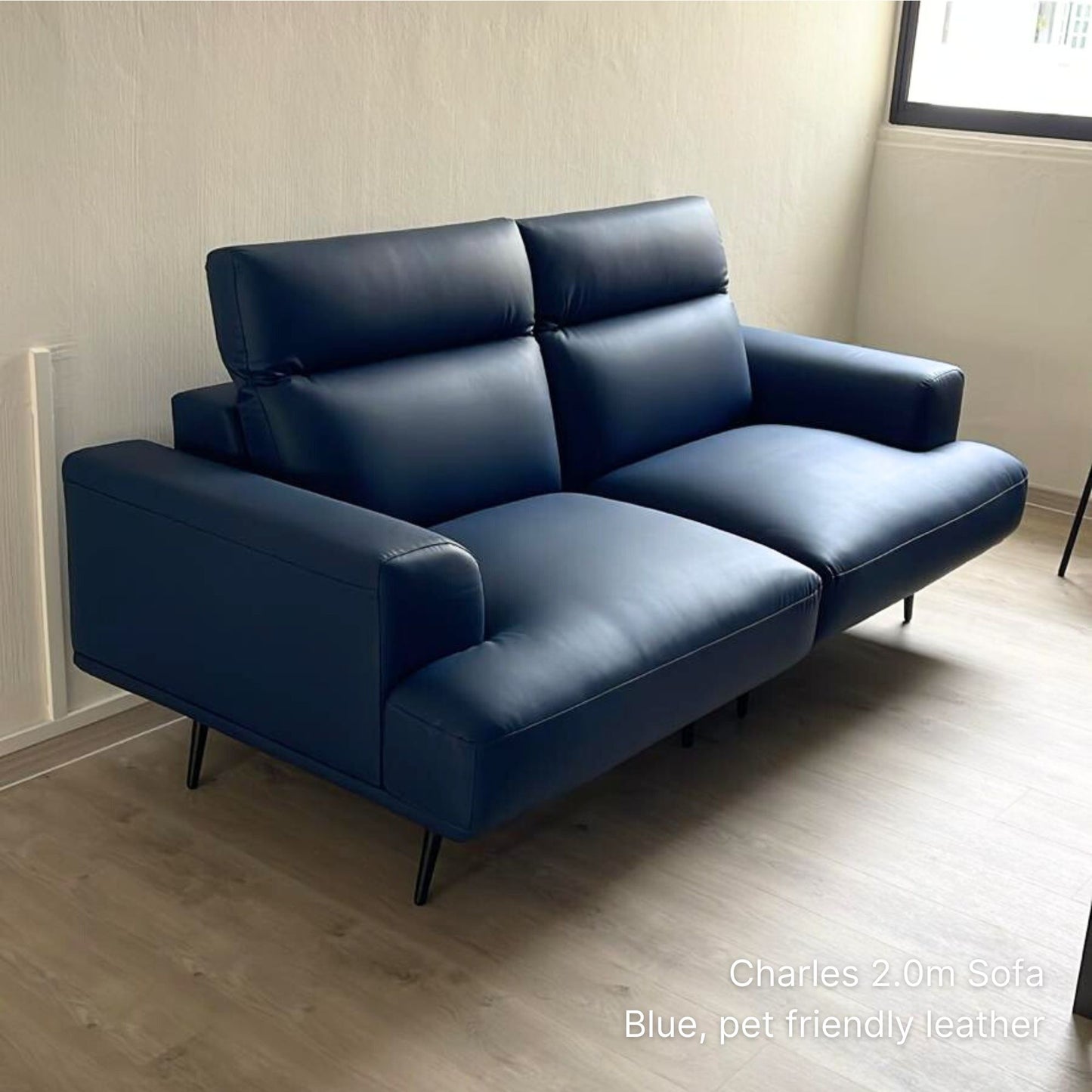 Blue Charles 3 seater 200cm faux leather sofa in a room with light wood flooring and a window.