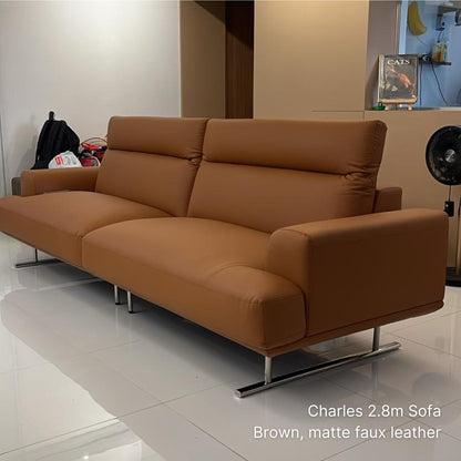 Brown sofa in a room with a fan and books on a shelf.