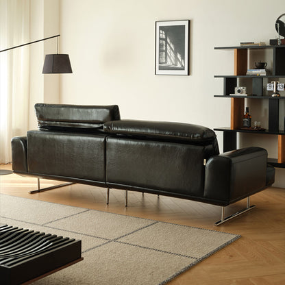 Modern black leather sofa in a living room setting with a rug and wall art.